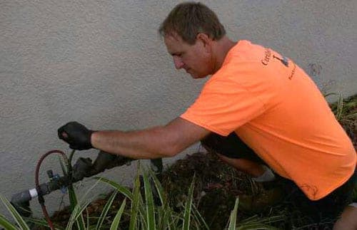 A Certified Backflow tester kneeling at a backflow preventer with the test gauge connected